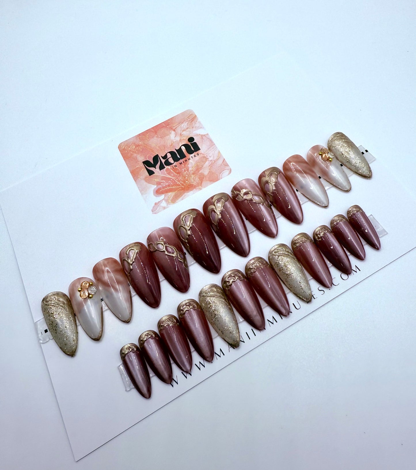 Set of almond shaped artificial nails with gold and 3D accents on a white background, featuring the brand 'Mani in Minutes.