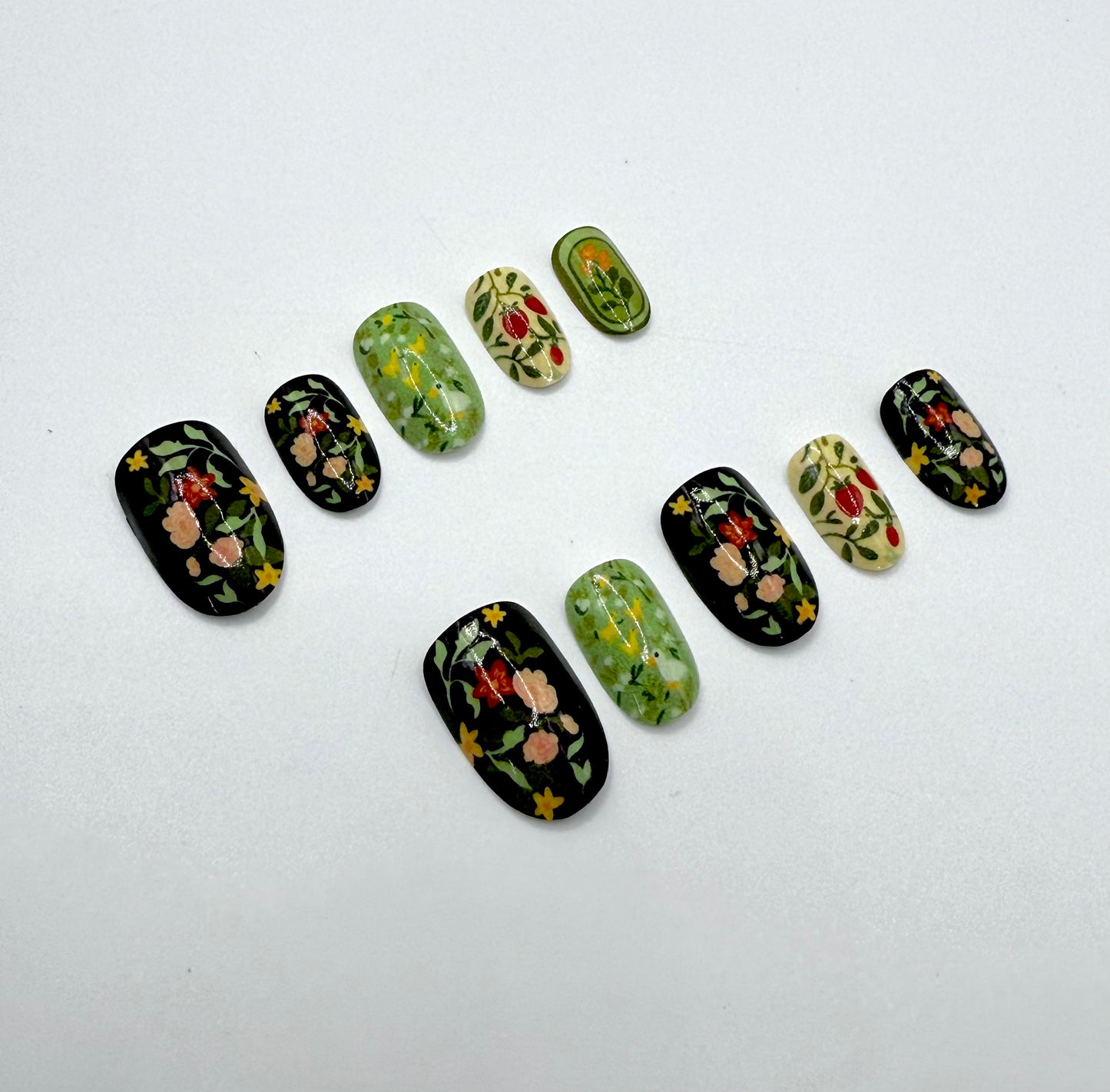 Close-up of Folk Garden press-on nails showing a mix of earthy green, black, and cream tones with detailed folk floral designs