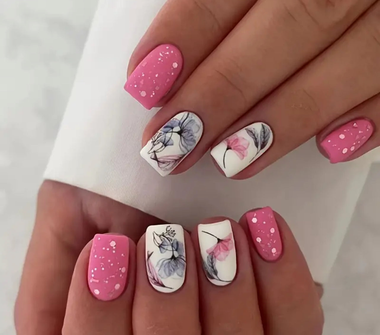 A set of press on nails featuring a floral design on a variety of nails, predominantly in pink color.