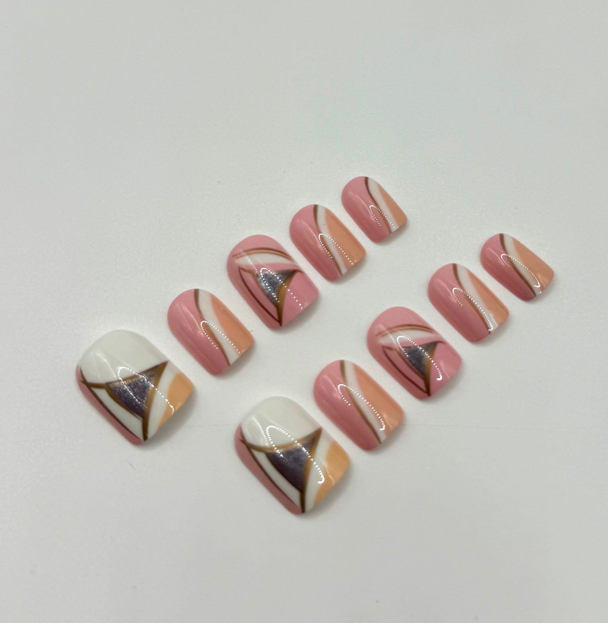 Close-up of Vogue Lines press-on nails showing modern geometric patterns in pink, white, peach, and silvery pewter