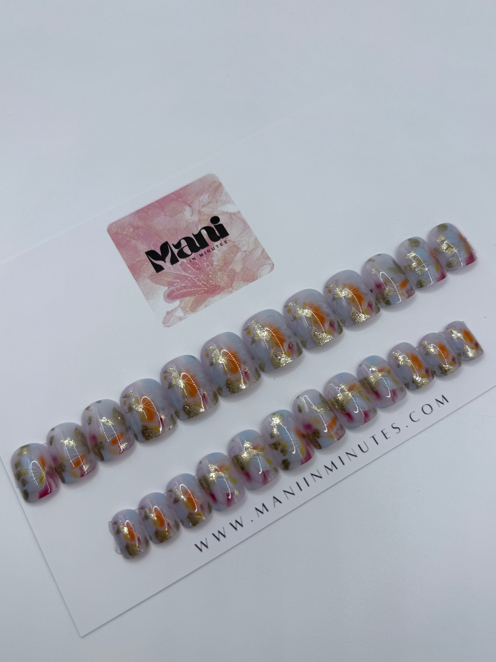 Colourful artistic nails with watercolour strokes and golden highlights on card. 